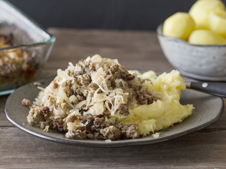 Ein grauer Teller mit dem Gericht auf einem rustikalen Holztisch. Alles von der Seite fotografiert.