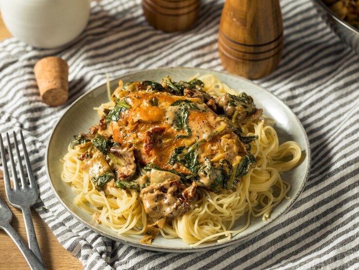 Toskanische Hähnchenpfanne mit Spaghetti, Spinat und getrockneten Tomaten auf weißem Teller.  | © iStock.com/bhofack2