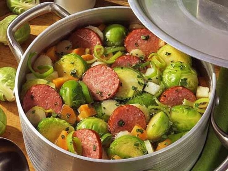 Der Rosenkohl-Eintopf mit Kabanossi sehr nahe und auf einem Holzbrett von schräg oben fotografiert.