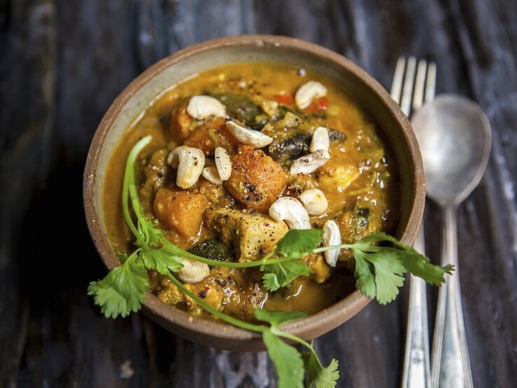 Cremiges Süßkartoffel-Curry mit Hähnchen und Cashews, garniert mit frischem Koriander in einer Schale auf dunklem Holztisch.