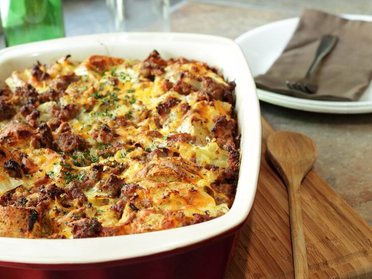 Brotauflauf mit Hackfleisch in Auflaufform auf Holzbrett.