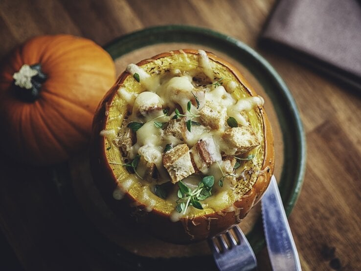 Draufsicht auf einen gefüllten Kürbis mit Kürbissuppe, überbacken mit Hackfleisch und Käse auf Holztisch. 