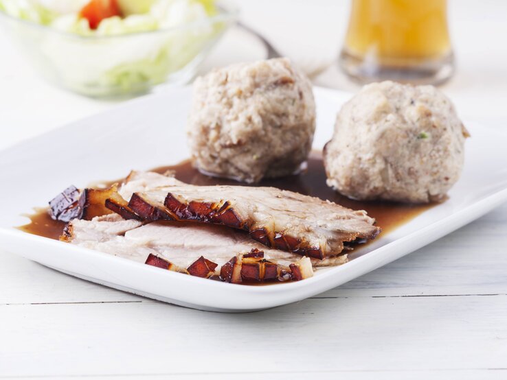 Ein weißer Holztisch mit weißem Teller und dem rustikalen Gericht darauf angerichtet. Alles von der Seite fotografiert.