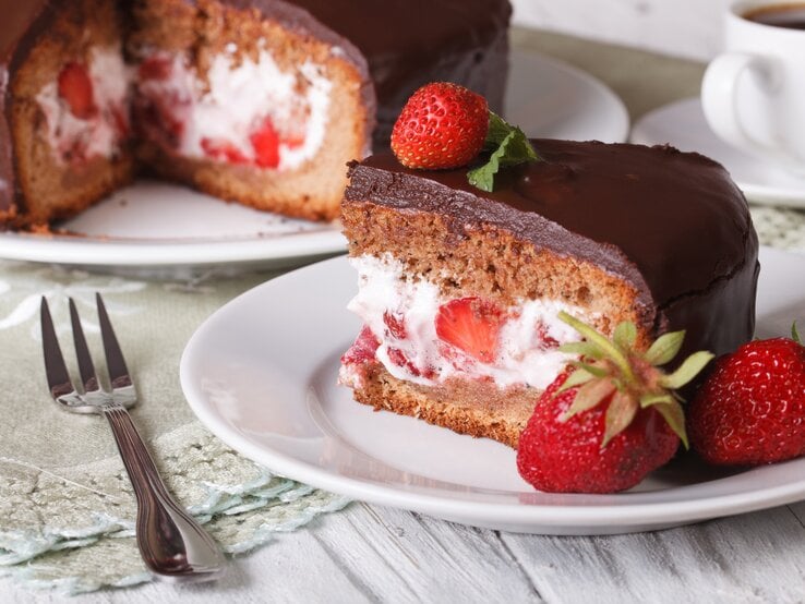 Schokoladenkuchen mit Schokolglasur und Erdbeer-Sahne-Füllung auf weißem Geschirr. 
