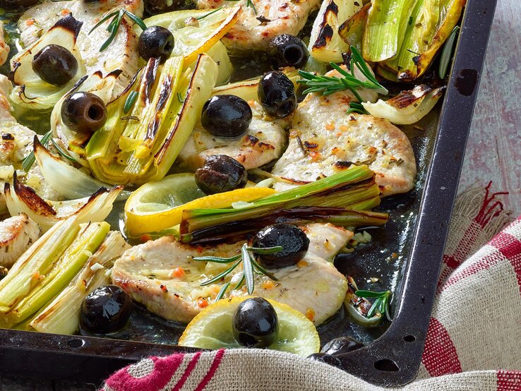 Zarte Hähnchenfilets mit schwarzen Oliven, Lauch, Fenchel, Zitrone und Rosmarin auf einem Blech goldbraun gebacken.