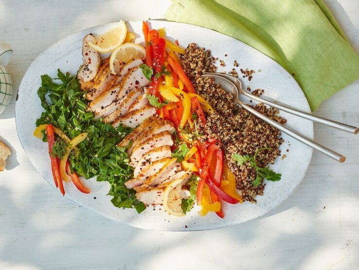 Quinoa-Hähnchen-Salat mit Rucola auf einem weißen Teller vor hellem Hintergrund, darauf ein grünes Tuch.