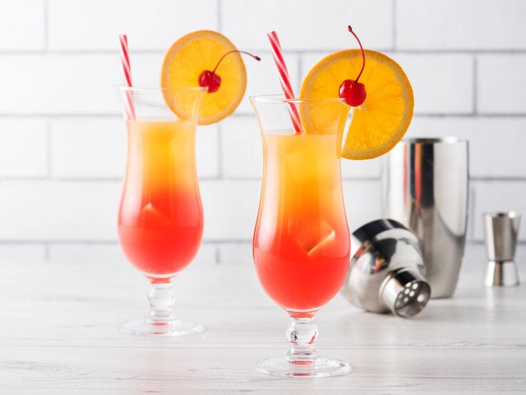 Zwei mit einer Orangenscheibe dekortiere Cocktails mit einem Farbverlauf von Rot zu Gelb, was an einen Sonnenaufgang erinnert.  | © imago stock&people