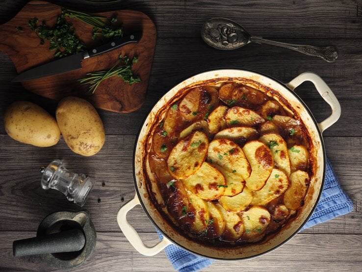 Eine runder Topf mit dem Gericht auf einem rustikalen Holztisch. Alles direkt von oben fotografiert.