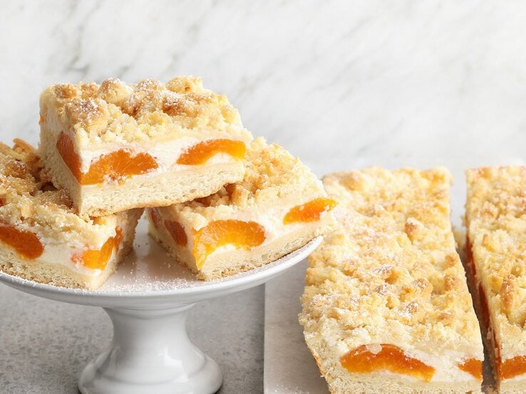 Mehrere Stücken des Aprikosen-Streuselkuchens auf hellem Marmoruntergrund. | © Seasons Agency / Gräfe & Unzer Verlag / Neubauer, Mathias