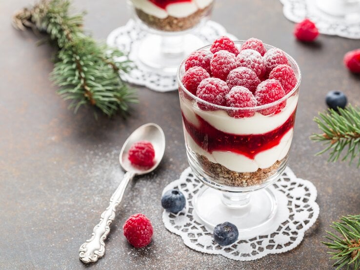 Dessert im Glas mit Himbeeren und Creme mit Kuchenboden auf dunklem Untergrund. Umgeben von Tannenzweigen. | © Shutterstock/Elena Elizarova