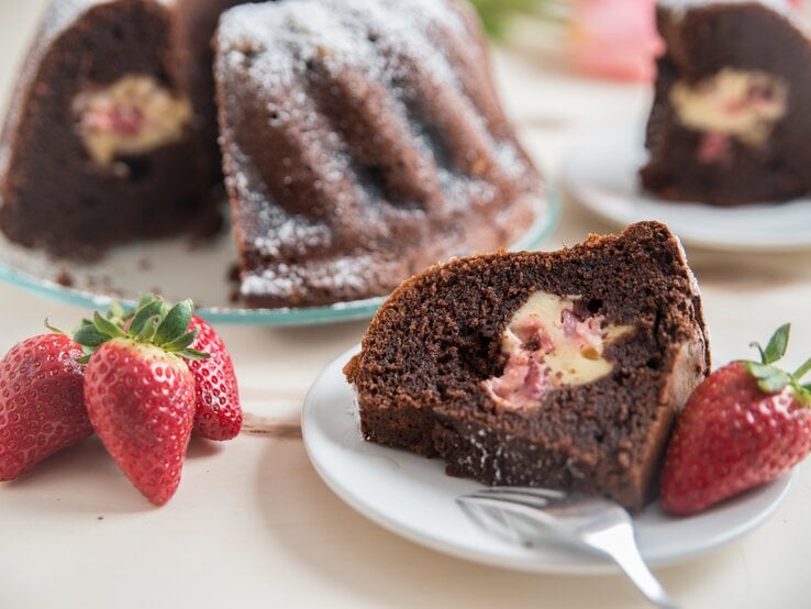 Mit Käsekuchen gefüllter Schokokuchen mit Erdbeeren auf weißem Teller.  | © Getty Images/A_Lein