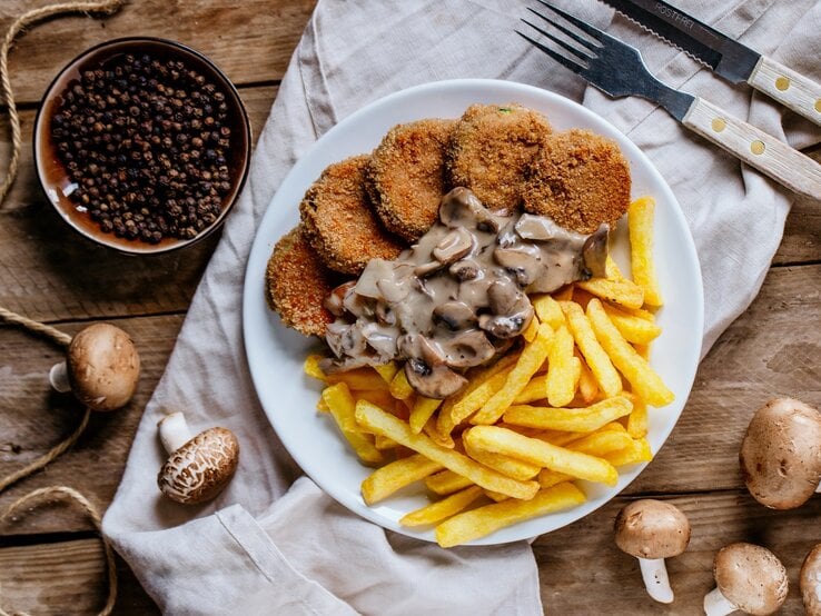 Jägerschnitzel mit Pilzsoße und Pommes / frische Pilze / Besteck / Küchentuch / Draufsicht