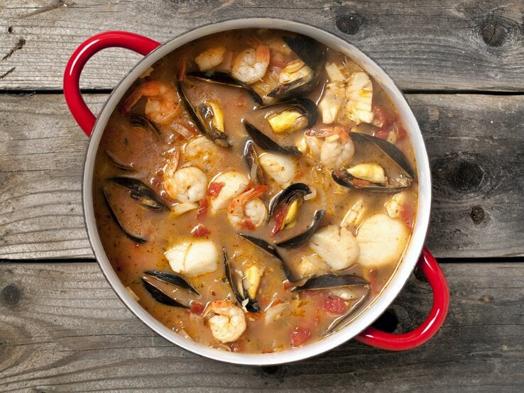 Eine köstliche Bouillabaisse mit Fisch, Muscheln, Gambas und Gemüse in einem Topf / Untergrund rustikaler Holzboden / Draufsicht