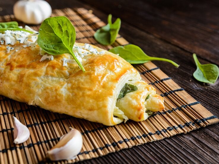 Seitliche Ansicht einer gebackenen Blätterteigrolle, gefüllt mit Spinat.