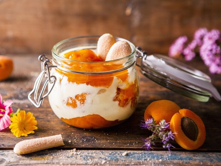 Aprikosen-Tiramisu in einem Einmachglas. Daneben verschiedene Zutaten und Blumen.