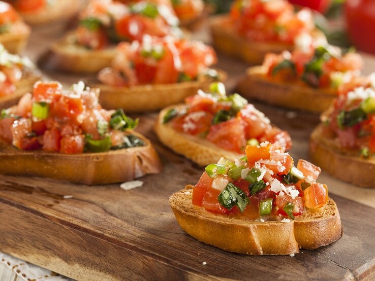 Mehrere Scheiben Weißbrot belegt mit frischen tomatenwürfeln auf einem Holzbrett.  | © iStock/ bhofack2