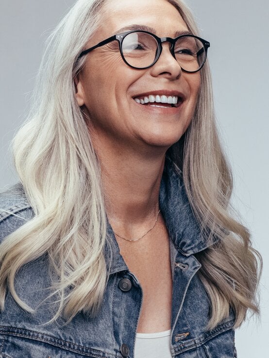 Reife Frau mit langen, grauen Haare mit leichten Wellen, die eine Brille trägt.  | © Shutterstock/Jacob Lund