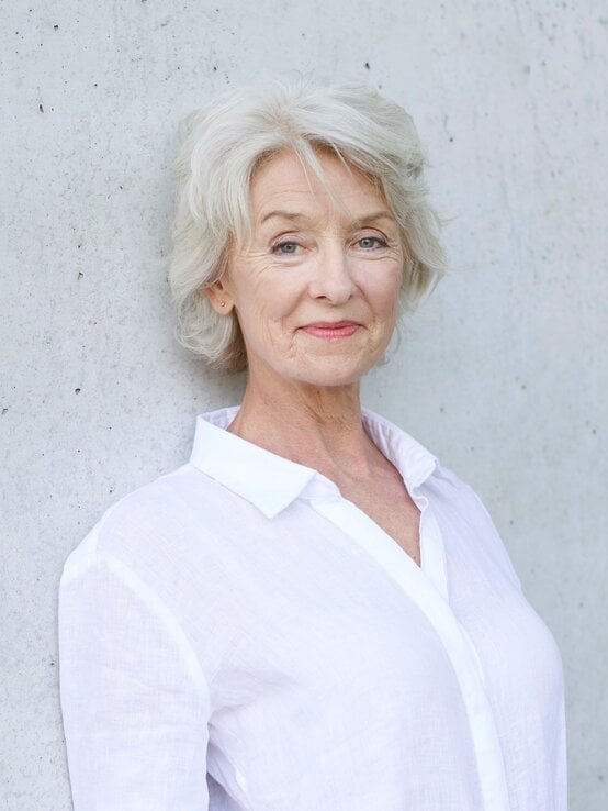 Frau mit grauen Haaren in weißer Bluse trägt eine Kurzhaarfrisur. | © Westend61 / Philipp Nemenz via Getty Images