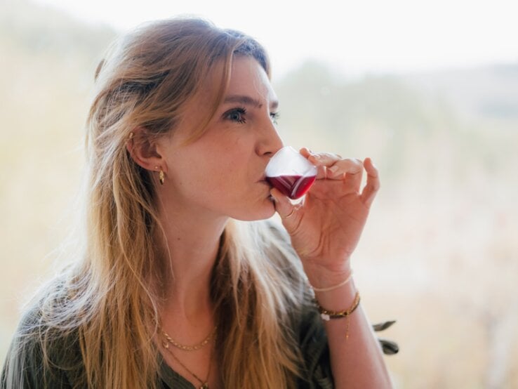 Blondhaarige Frau trinkt genüsslich den Saft EisenPlus vor einem hellen, verschwommenen Waldpanorama.