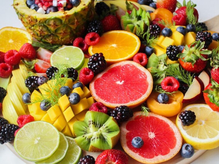 Bunt angerichtete Obstplatte mit frischen Früchten wie Grapefruit, Orange, Kiwi, Mango, Beeren, Erdbeeren, Limetten und Ananas; gesunde, farbenfrohe Vitaminquelle für Ernährung und Fitness.
