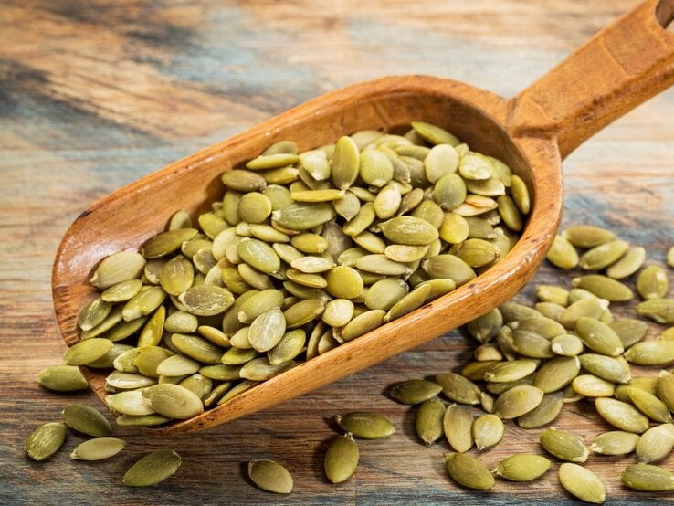 Holzschaufel mit grünen Kürbiskernen auf rustikalem Untergrund. | © Getty Images Pro/ marekuliasz via Canva.com