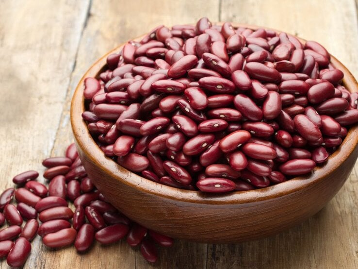 Holzschale voller roter Kidneybohnen, einige Bohnen daneben verstreut. | © Tarakorn arunothai via Canva.com 