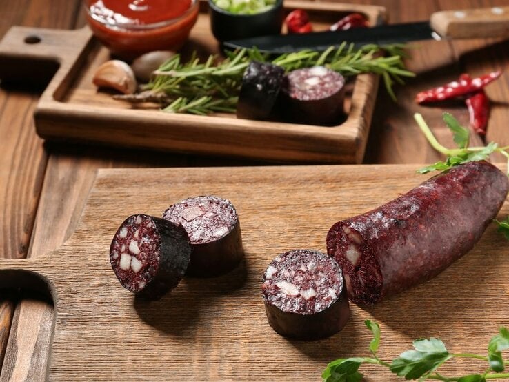 Aufgeschnittene Blutwurst auf Holzbrett mit Kräutern und Dips im Hintergrund. | © pixelshot via Canva.com 