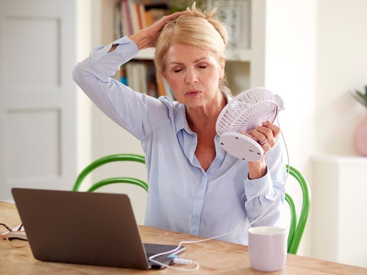 Ältere Dame ist heiß und sie hat einen kleinen Ventilator in der Hand und nimmt ihre Haare hoch | © adobe.stock.com/Monkey Business 