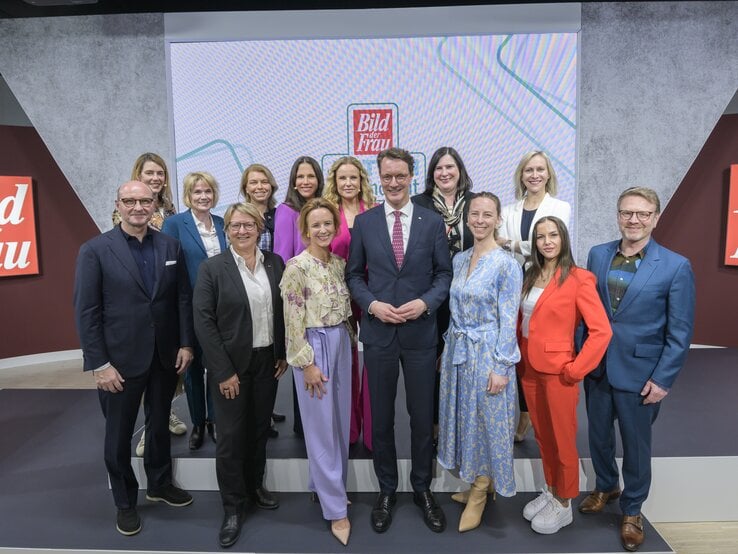Vierzehn Frauen und zwei Männer in Businesskleidung posieren lächelnd auf einer Bühne vor „Bild der Frau“-Logos.