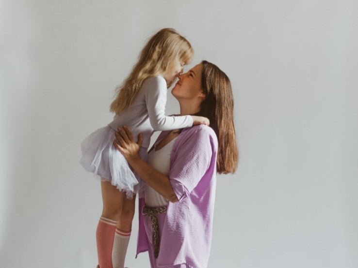Junge Frau mit dunklen Haaren umarmt ihre kleine Tochter. 