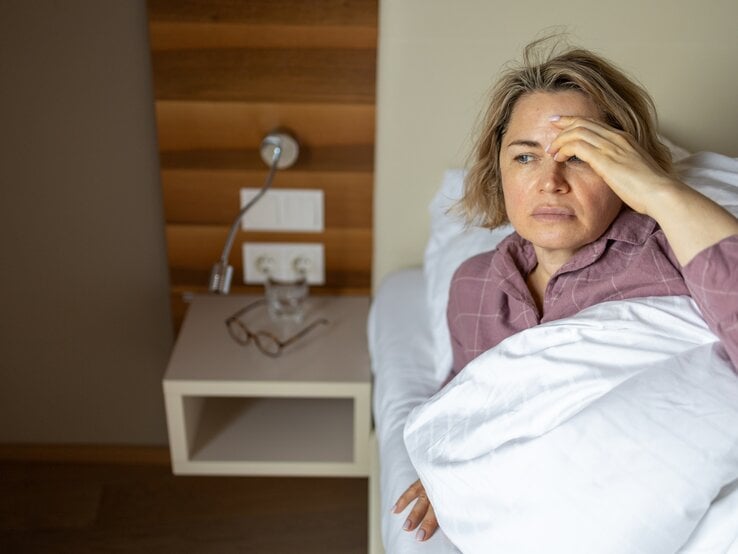 Frau liegt im Bett, ihre Stirn glänzt.
