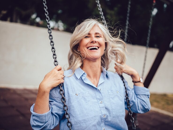 Frau sitzt auf einer Schaukel und lacht.