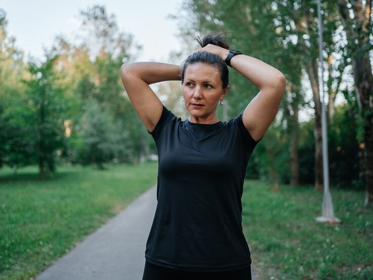 Frau über 45 bindet sich die Haare zum Zopf, ihre Stirn glänzt.