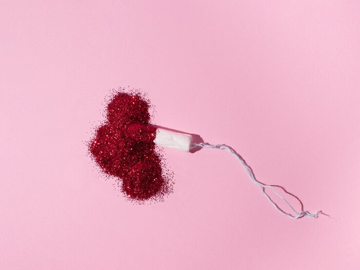 Tampon liegt auf rosa Untergrund in einem Haufen aus rotem Glitzer.
