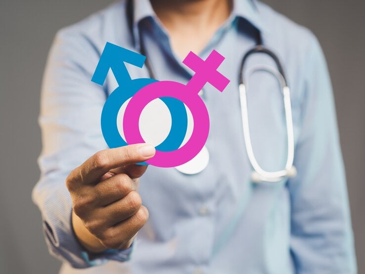 Ein Arzt hält die Symbole für das männliche und weibliche Geschlecht in den Händen.