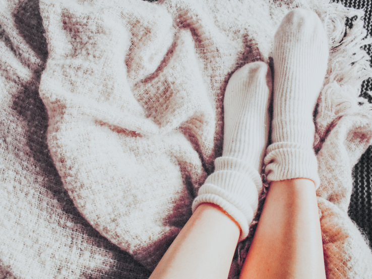 Zwei gepflegte Füße in kuscheligen Wollsocken stehen auf bunt gefärbtem Herbstlaub.