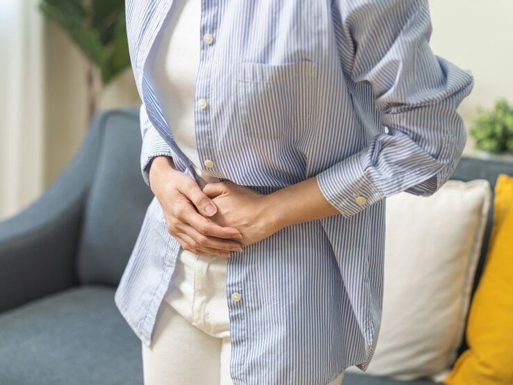 Junge Frau schaut zu ihrem aufgeblähtem Bauch und fasst diesen an.