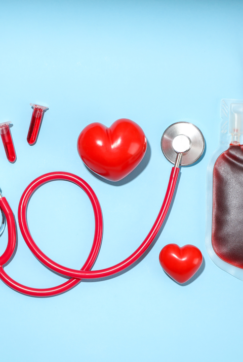 Medizinisches Stethoskop, ein Blutbeutel, zwei Blutprobenröhrchen und zwei rote Herzmodelle auf blauem Hintergrund arrangiert.