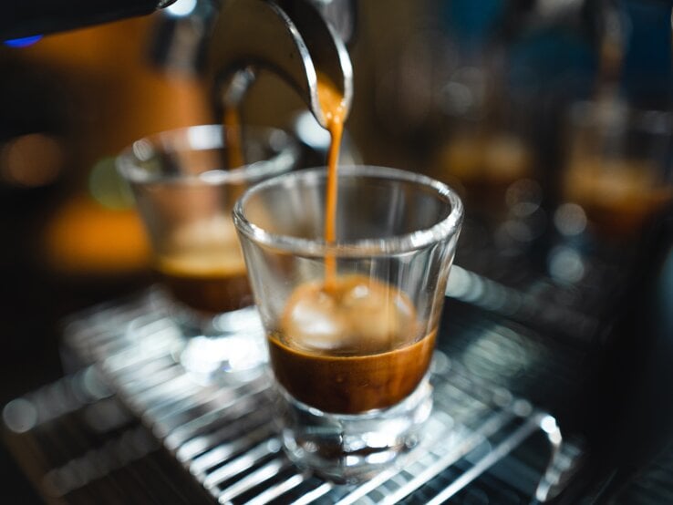 Frischer Espresso strömt geschmeidig aus einem Siebträger in ein transparentes Glas auf einem Metallgitter.