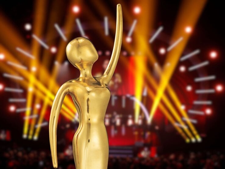 Glänzende Preisfigur in abstrakter Form steht vor strahlenden Lichtstrahlen auf festlich beleuchteter Showbühne.