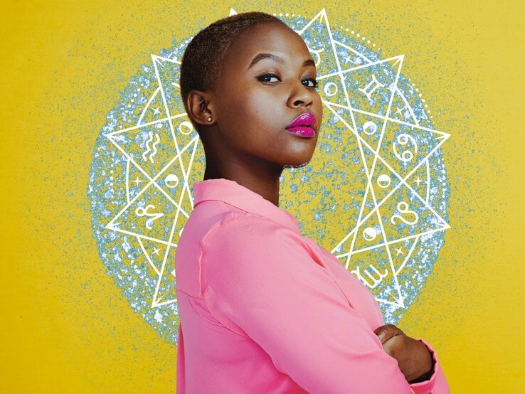 Eine selbstbewusste Frau mit kurz geschnittenem Haar steht vor einem gelben Hintergrund mit einem großen astrologischen Rad. Sie trägt eine leuchtend rosa Bluse und hat die Arme verschränkt. Ihr Gesichtsausdruck ist ernst und bestimmt, und ihre Lippen sind mit glänzendem, pinkem Lippenstift geschminkt.