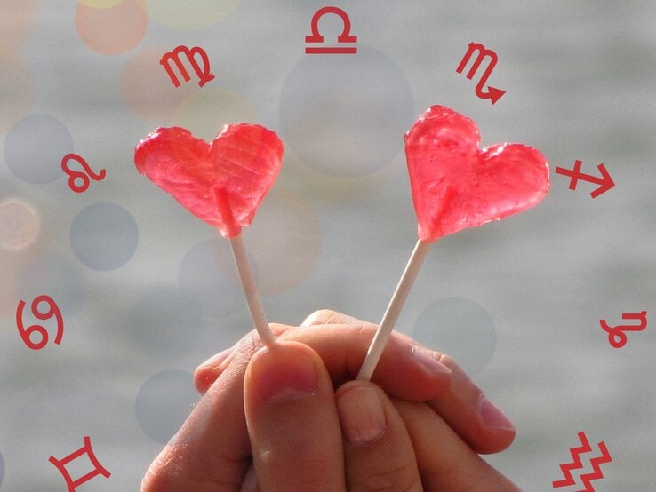 Das Bild zeigt zwei Hände, die zwei herzförmige, rote Lutscher halten. Im Hintergrund sind verschwommene, bunte Kreise zu sehen. Um die Lutscher herum sind rote astrologische Symbole verteilt, die verschiedene Sternzeichen darstellen, darunter Löwe, Jungfrau, Waage, Skorpion, Schütze, Wassermann, Zwillinge und Krebs.