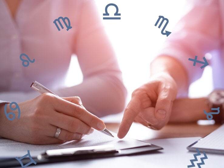 Zwei Personen in Business-Kleidung sind in ein Gespräch vertieft und arbeiten an einem Dokument. Die Hände einer Person halten einen Stift und zeigen auf das Papier, während die andere Person etwas darauf zeigt. Um das Bild herum sind verschiedene astrologische Symbole verstreut, darunter Symbole für Löwe, Jungfrau, Waage, Skorpion, Schütze, Steinbock, Wassermann und Fische. Die Szene ist in weichem Licht gehalten und hat eine professionelle Atmosphäre.