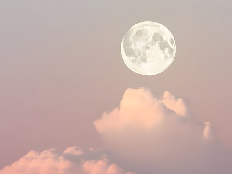 Das Bild zeigt den Vollmond, der am Himmel über pastellfarbenen Wolken schwebt. Der Himmel hat eine weiche Farbpalette aus Rosa und Lavendel, die eine friedliche und ruhige Atmosphäre schafft. Der Mond ist klar und detailreich sichtbar, und die Wolken darunter erscheinen flauschig und leicht, was dem Bild einen träumerischen Charakter verleiht.