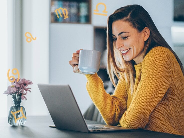 Eine Frau mit langen, braunen Haaren sitzt lächelnd an einem Tisch und schaut auf einen Laptop. Sie trägt einen gelben Pullover und hält eine Tasse in der Hand. Auf dem Tisch steht eine kleine Vase mit lila Blumen. Um sie herum schweben astrologische Symbole, die verschiedene Sternzeichen darstellen. Die Umgebung deutet auf eine gemütliche Wohnsituation hin, möglicherweise eine Küche oder ein Wohnzimmer im Hintergrund.