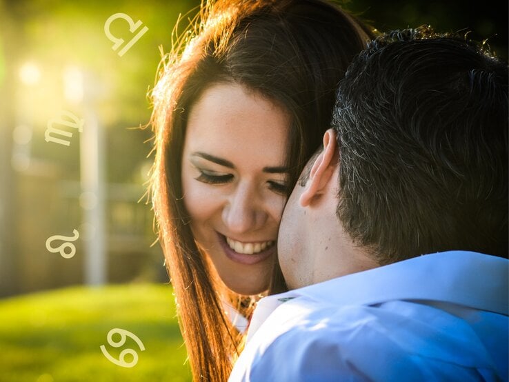 Ein lächelndes Paar, das sich im Freien umarmt. Die Frau mit langen braunen Haaren lächelt und schließt die Augen, während der Mann mit dunklem Haar ihr nahe ist. Im Hintergrund sind die astrologischen Symbole für Löwe, Jungfrau, Waage und Krebs in einem verschwommenen Grün eingebettet.