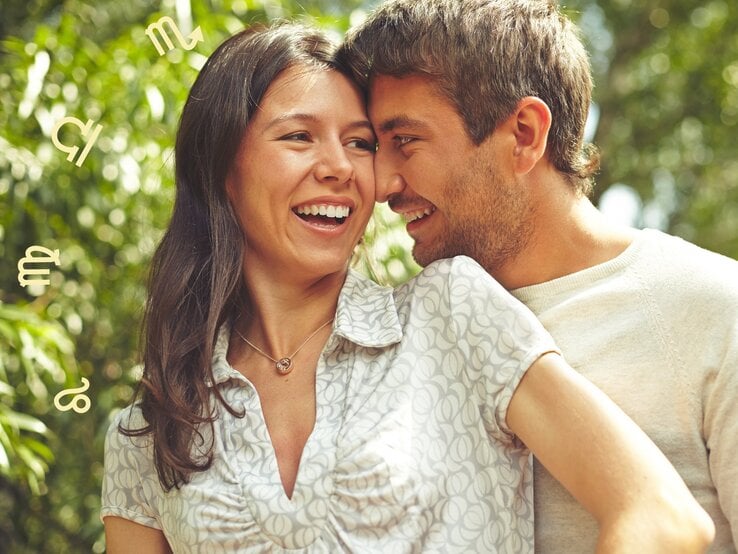 Das Bild zeigt ein glückliches Paar, das sich lachend und liebevoll ansieht, während sie sich gegenseitig umarmen. Im Hintergrund sind grüne Blätter und Bäume zu sehen, die eine natürliche und entspannte Atmosphäre schaffen. Um das Paar herum schweben verschiedene astrologische Symbole, was auf einen Zusammenhang mit Horoskopen oder Sternzeichen hinweist. Die Frau trägt ein gemustertes Oberteil und eine Halskette, während der Mann ein helles Langarmshirt trägt. Beide wirken entspannt und glücklich, was die positive Stimmung des Bildes unterstreicht.