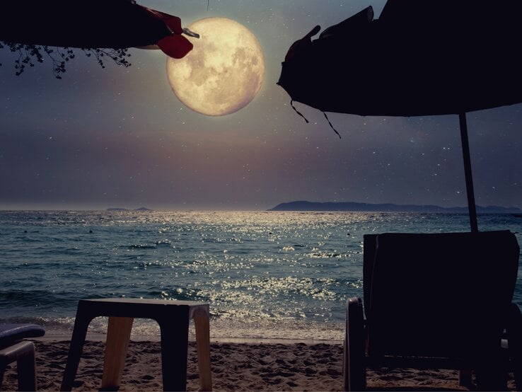 Ein ruhiger Strand, beleuchtet vom sanften Schein des Vollmonds, der majestätisch über dem Horizont aufsteigt. Der Mond wirft sein silbriges Licht auf das Meer, das sanft in kleinen Wellen an den Strand spült und dabei glitzernde Reflexionen auf der Wasseroberfläche erzeugt. Im Vordergrund stehen zwei Liegestühle und ein kleiner Tisch, die unter den Schatten von großen Sonnenschirmen verborgen sind. Der Strand ist leer und still, die Atmosphäre ruhig und verträumt, als ob die Welt für einen Moment innehält, um die Magie dieser Mondnacht zu genießen. Die entfernten Inseln am Horizont wirken wie stille Wächter dieser friedlichen Szene. Es ist ein Moment der Besinnung, des Innehaltens und des Einsseins mit der Natur.