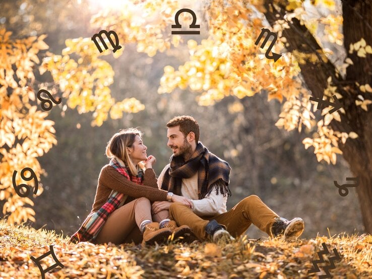  Das Bild zeigt ein Pärchen, das in einer herbstlichen Landschaft unter einem Baum sitzt. Die beiden blicken sich lächelnd an und wirken vertraut und glücklich miteinander. Sie sind warm gekleidet und umgeben von gelb-orangefarbenen Blättern, die die gemütliche Herbstatmosphäre betonen. Rund um die Szene sind Symbole der Sternzeichen wie Widder, Löwe, Waage und andere zu sehen, die das Bild mit einem astrologischen Thema verbinden.