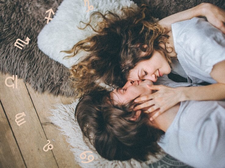 Ein Paar liegt kuschelnd auf einem Teppich, ihre Gesichter sanft aneinander, während sie sich zärtlich berühren. Um sie herum sind astrologische Symbole verstreut, die eine romantische und mystische Stimmung hervorrufen.